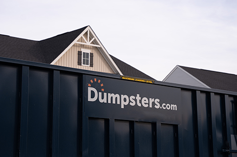 Close up image of blue dumpster in front of house with Dumpsters.com logo.