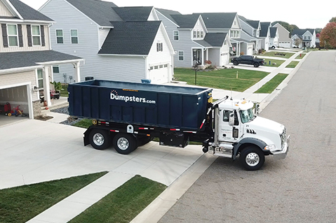 Dumpsters.com truck hauling a roll off dumpster through a neighborhood.