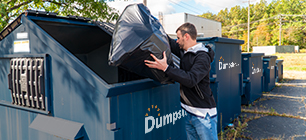 Business owner tossing trash in Dumpsters.com front load dumpster.