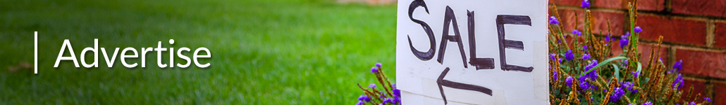 Sale Sign with an Arrow in Front of Flowers and a Brick Wall.