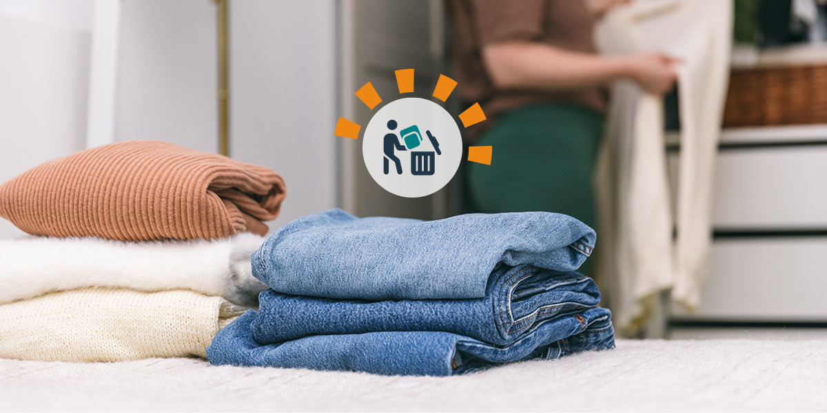 A woman clearing out her closet with jeans and sweaters laying on the bed. 