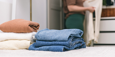 A woman clearing out her closet with jeans and sweaters laying on the bed. 