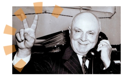 George Roby Dempster holding a phone in one hand and making a peace sign with the other.