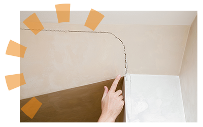 A hand pointing at a crack on a tan wall being held up by a white support beam.