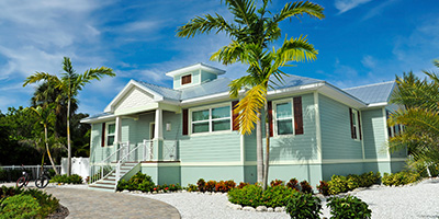 Blue vacation home with palm trees and gravel landscaping underneath clear blue sky.