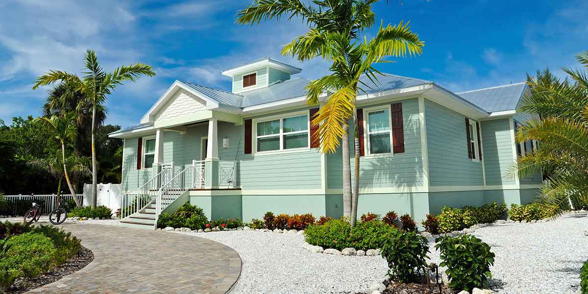 Blue Vacation Home with Palm Trees and Gravel Landscaping Underneath Clear Blue Sky.