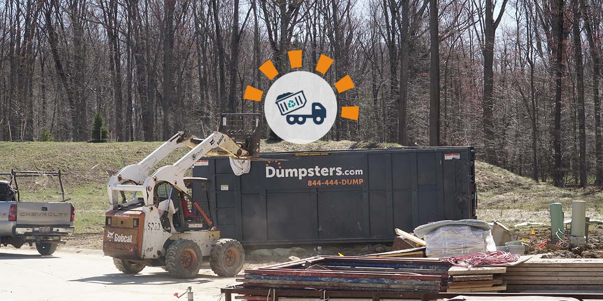 Pickup truck near a bobcat dumping debris in a blue roll off dumpster.