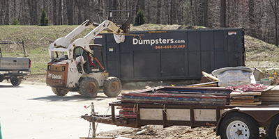 A Bobcat drives toward a blue Dumpsters.com roll off dumpster.