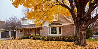 Brick and vinyl house in fall before winter with lawn covered leaves homeowner checklist.