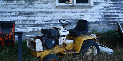 A broken riding lawn mower sitting in overgrown grass.