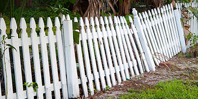 Old broken white fence leaning over needing removal.