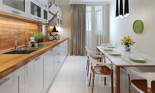 Side view of galley kitchen with wood countertops, white cabinets and a table set with flowers.