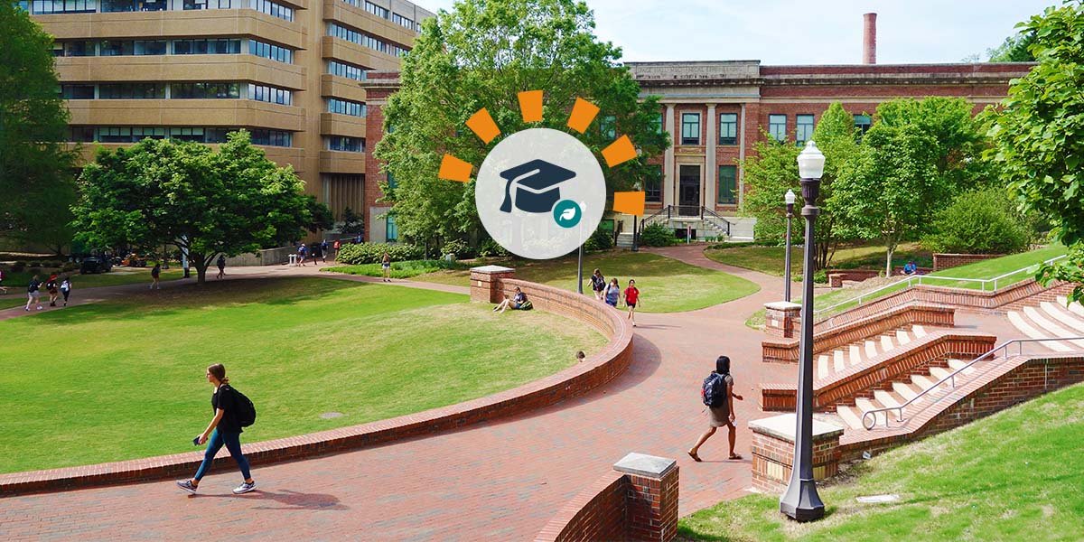 Students walking on the sidewalk of a campus green with a brick domed building in the background.