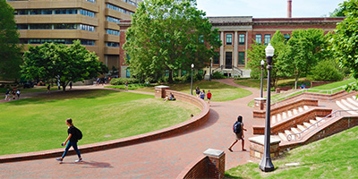 Students walking on the sidewalk of a campus green with a brick domed building in the background.
