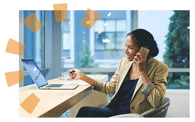 A woman talking on the phone in front of a computer with a pen in her hand.