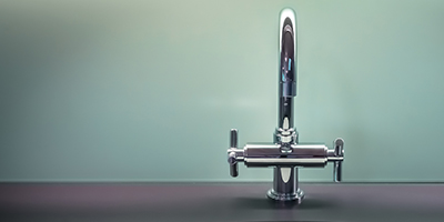 A chrome faucet on a black counter with green walls. 