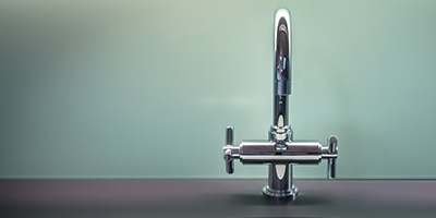 A chrome faucet on a black counter with green walls.