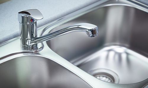 A chrome finished faucet and handle in a double-basin kitchen sink.