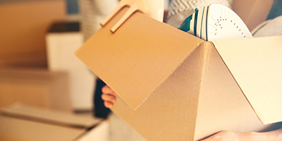 a person carrying a cardboard box full of items out of their home. 