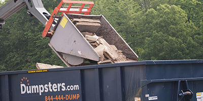 Crane dumping wood into a roll off Dumpsters.com dumpster.
