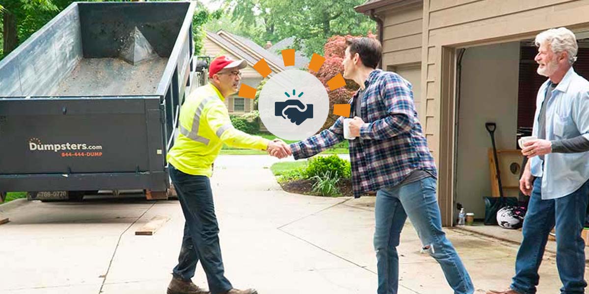 A Dumpsters.com delivery driver shakes hands with a customer during a delivery.
