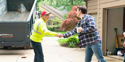 A Dumpsters.com delivery driver shakes hands with a customer during a delivery.