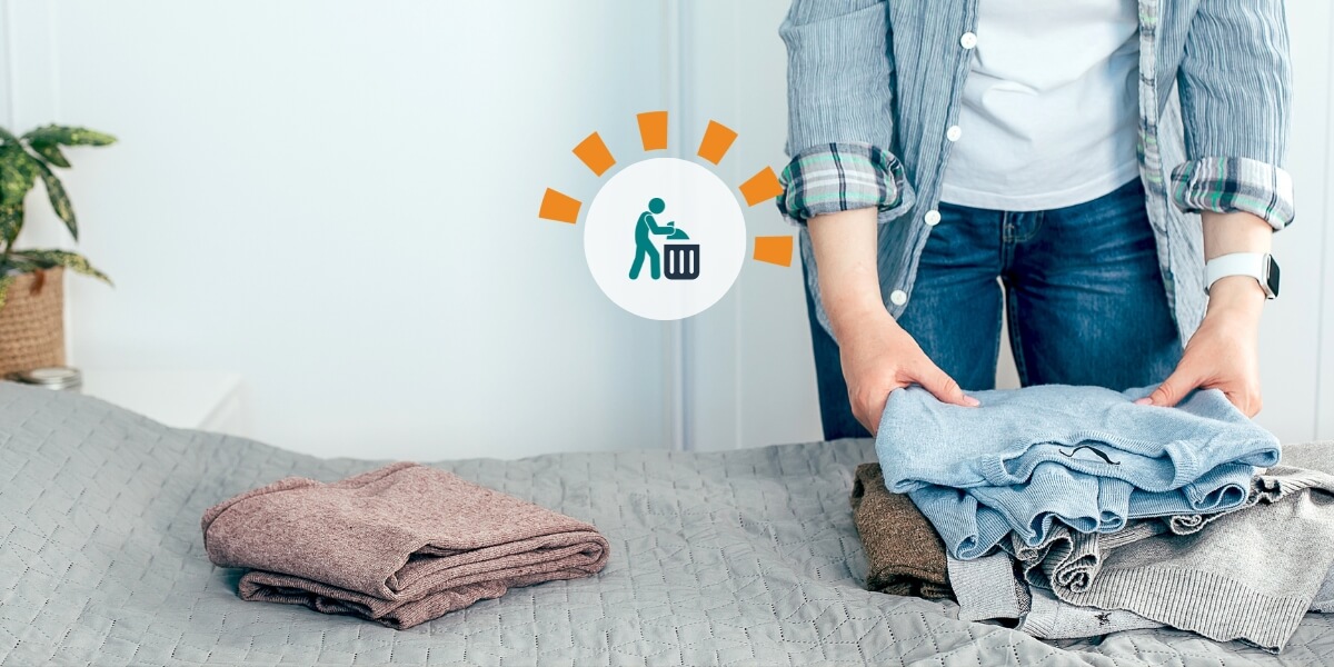 A woman clearing out her closet with jeans and sweaters laying on the bed. 
