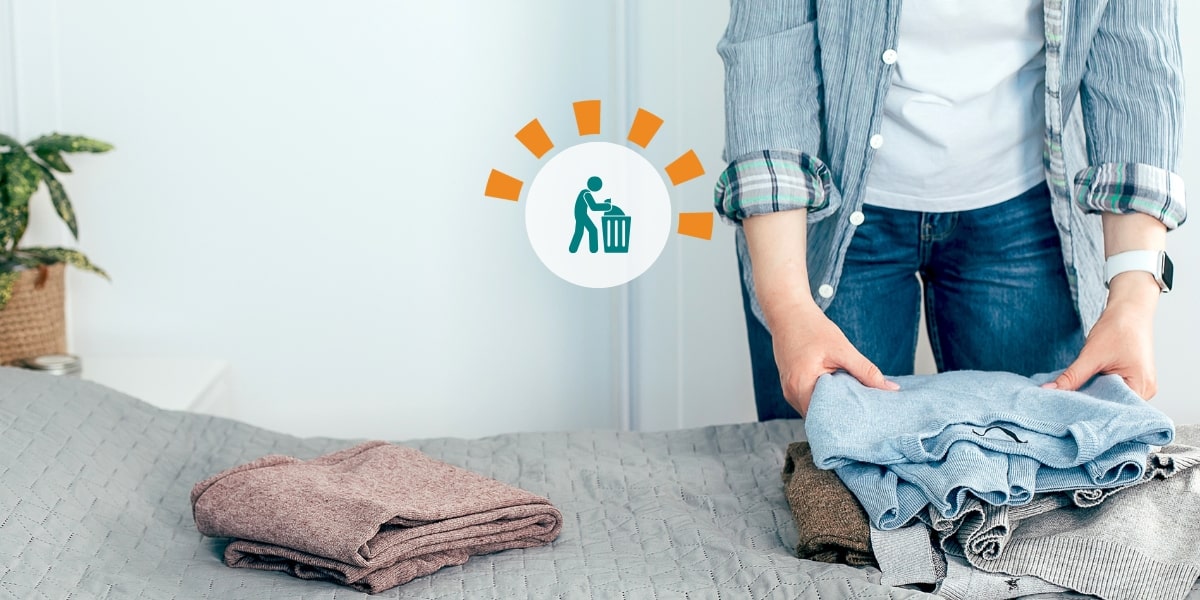 A woman clearing out her closet with jeans and sweaters laying on the bed.