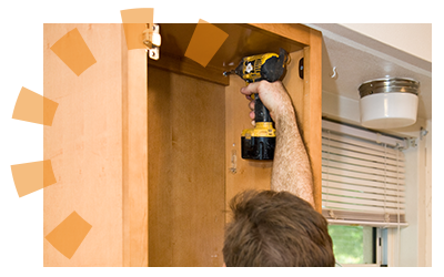 A man uses a drill with a screwdriver attachment to unscrew a cabinet from a kitchen wall.
