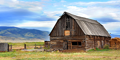 A decaying barn in a grassy field with blue skies. 