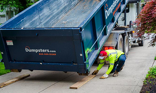 Driver Laying Down Wood Under Roll Off Dumpster.