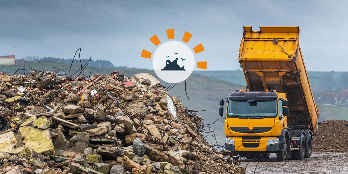 Orange dump truck tipping load into a landfill with debris in the foreground.