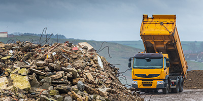 Orange dump truck tipping load into a landfill with debris in the foreground.
