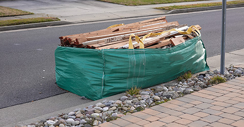 A dumpster bag filled with scraps sitting on the side of a street
