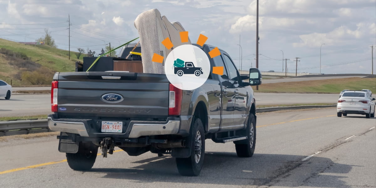 A pickup truck carrying a mattress and two pieces of furniture secured with ropes.