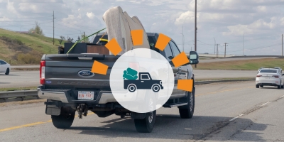 A pickup truck carrying a mattress and two pieces of furniture secured with ropes.