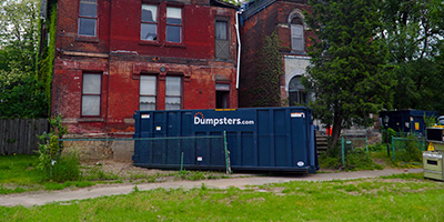 Dumpsters.com roll off dumpster in front of two brick homes.