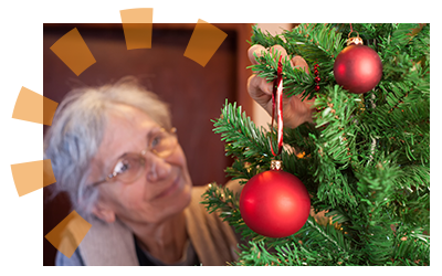 An older woman decorating an artificial Christmas tree with a red ornament. 
