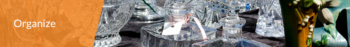 White text 'Organize' over image of an estate sale with crystal vases, jars, candle holders, bowls and cake trays.