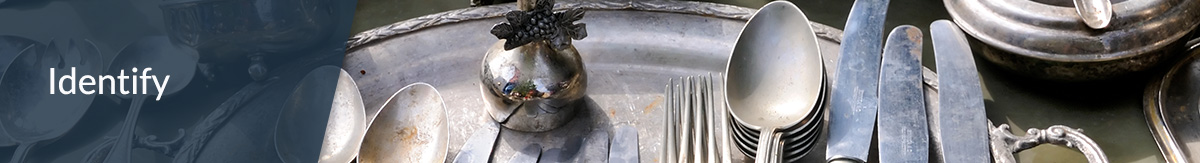 White text 'Identify' over image of a table of antique silverware, silver tray, jewlery boxes, bowls and cups at an estate sale.