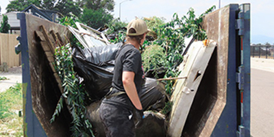 Extreme Community Makeover volunteer loading debris into a full Dumpsters.com dumpster