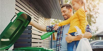 A father and daughter properly recycling materials outside. 