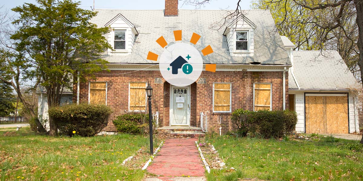 A foreclosed property with boarded up windows and doors and an overgrown yard.