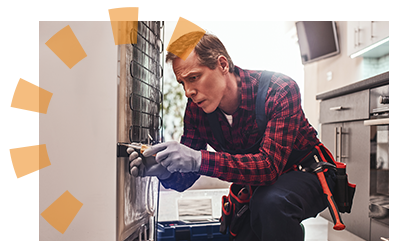 A man in a plaid shirt and grey gloves using a yellow screwdriver on the back of a refrigerator.
