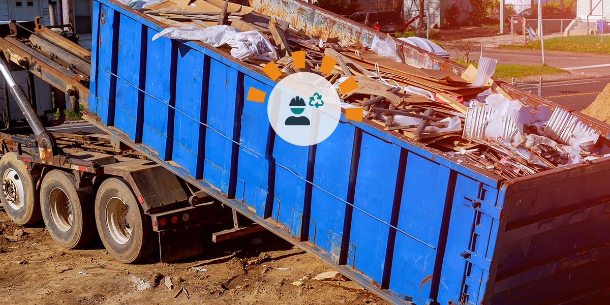 A blue roll off dumpster being loaded onto the back of a dump truck.