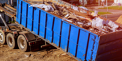 Full, blue dumpster being loaded onto the back of a truck.