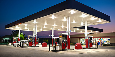 A gas station with it's lights turned on as the sun sets behind it.