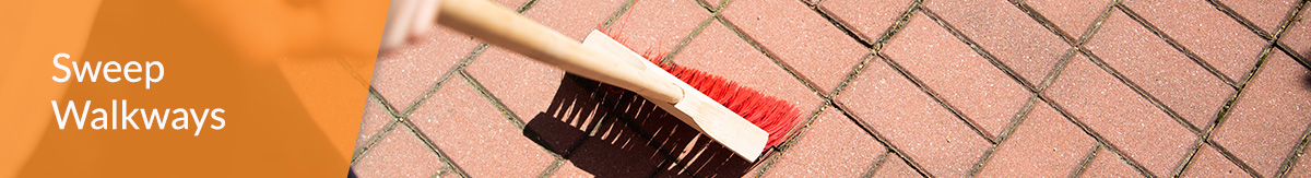 An employee sweeps a brick walkway outside a store.