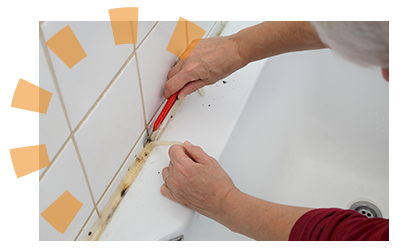 A person removing the surrounding caulk from a bathtub.