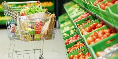 Full Shopping Cart Next to Green Bins of Produce at a Grocery Store